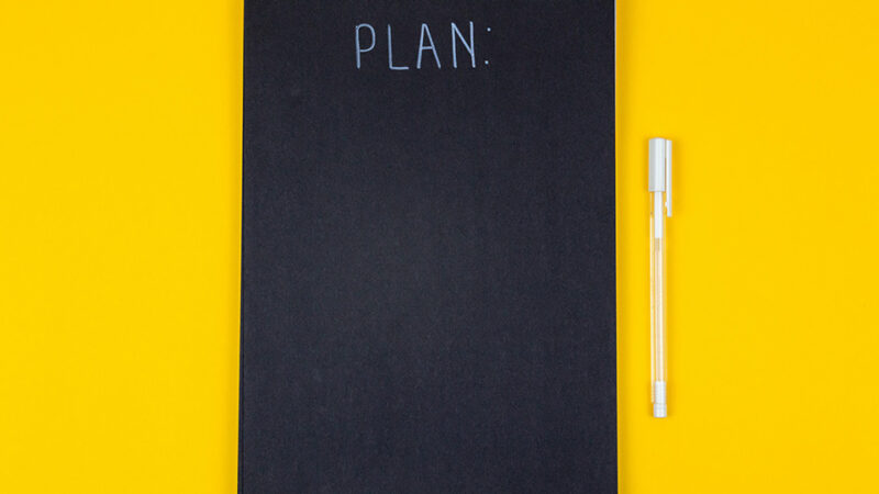 Notebook and pen. The notebook has the text "PLAN" on the front.